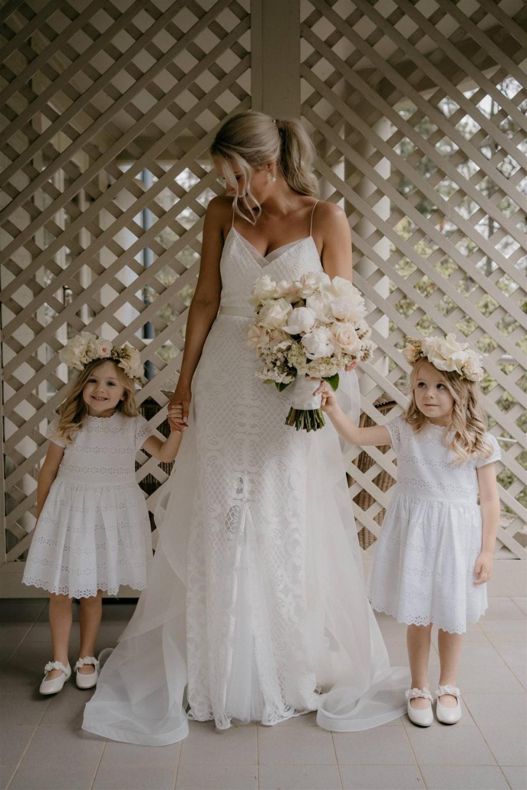 KWH bride Ashleigh with her two flower girls, holding her pink and white florals wearing the Elodie gown, a lattice lace wedding dress with spaghetti straps.