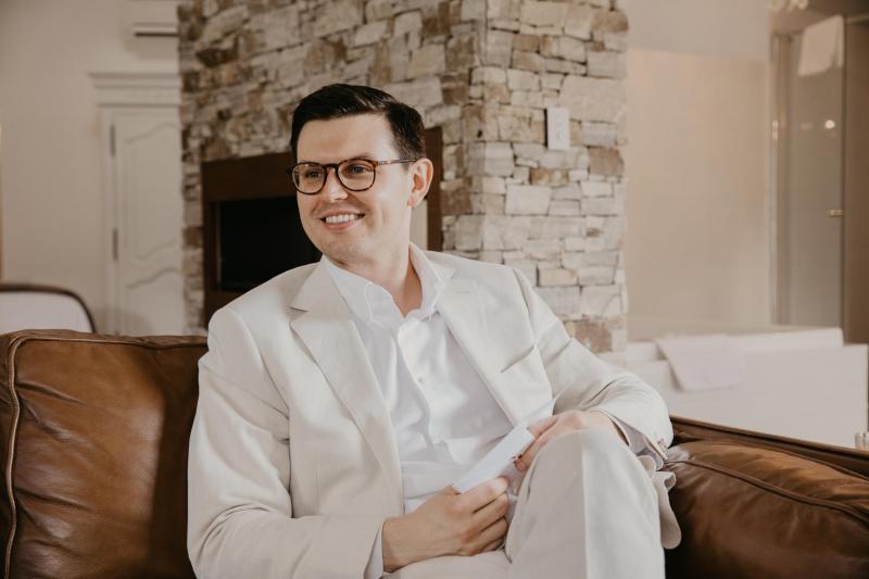 Leah's husband Sam smiling in white wedding suit.