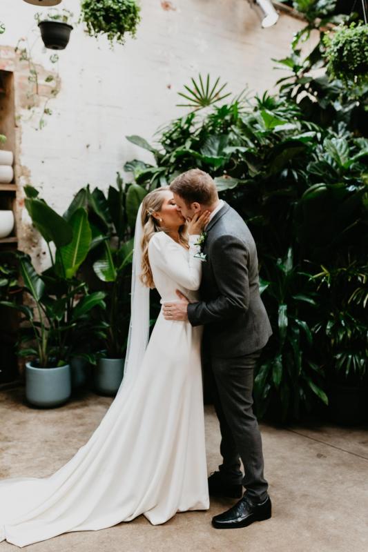 KWH bride Kara kissing husband Justin at wedding ceremony, wearing the AUBREY gown; a long-sleeve euphorbia wedding dress with a deep v-neck.