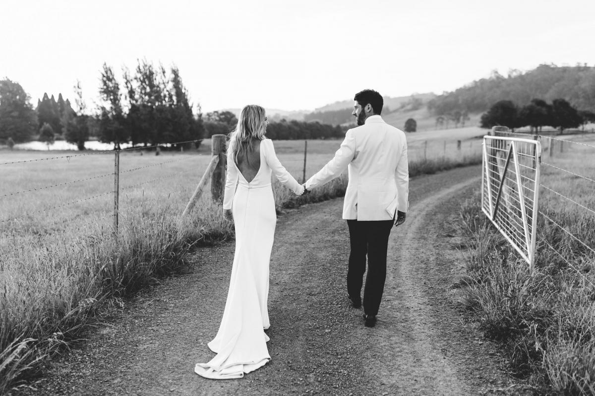 Real bride Annabelle with husband Marc on open country road at farm wedding, bride wearing the timeless Aubrey dress with long sleeves and a deep V back.