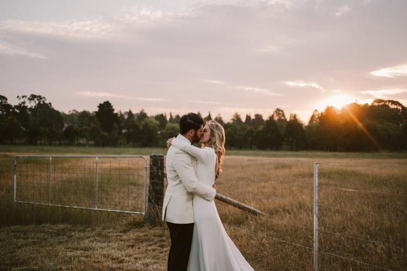 Real bride Annabelle & husband Marc sunset kiss at country farm wedding, bride wearing the long sleeve Aubrey wedding dress by Karen Willis Holmes.