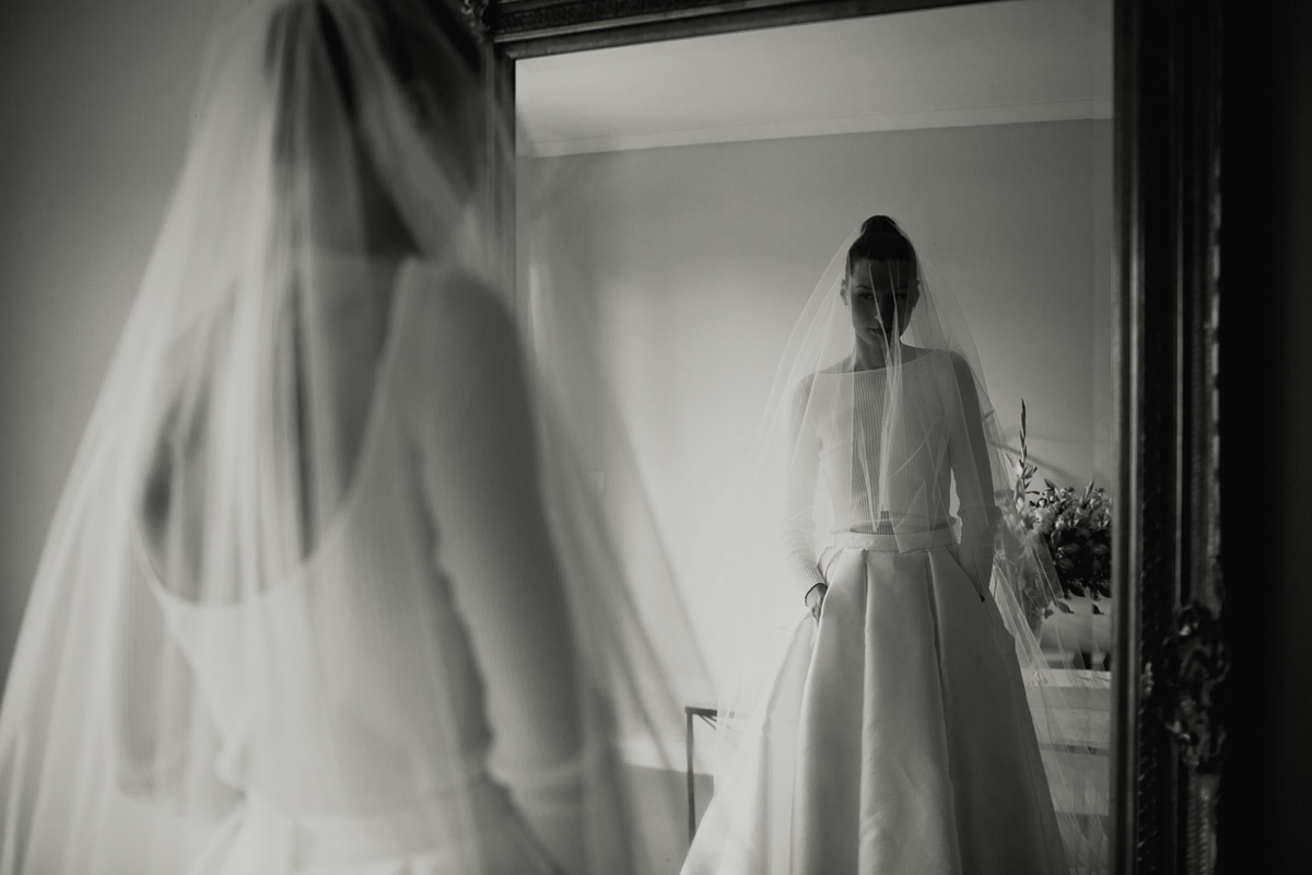 Bride admires herself in Bespoke Melanie wedding skirt by Karen Willis Holmes with veil over the face