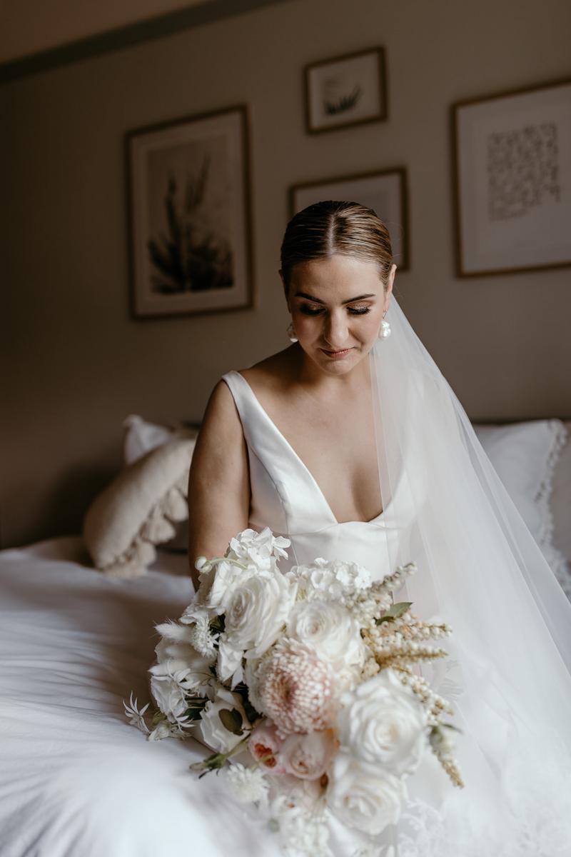 Close up of bride admiring flowers in made to order bespoke wedding dress Taryn Camille by Karen Willis Holmes