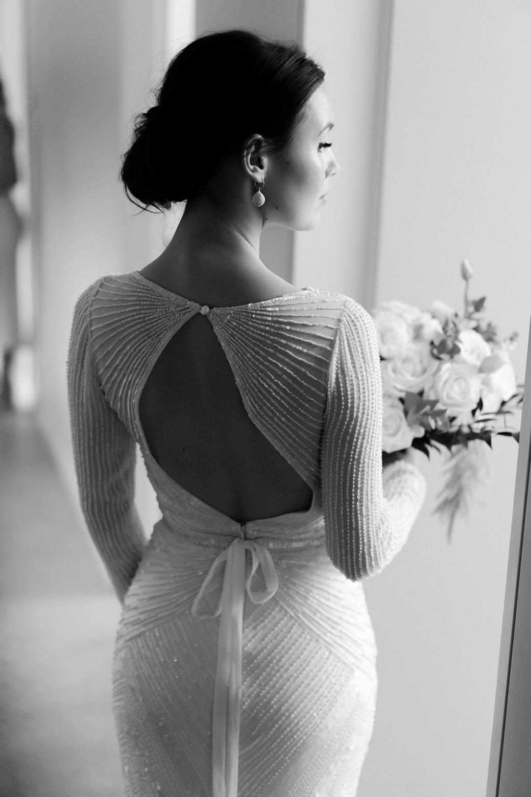 B&W image of Karen Willis Holmes bride Anna wearing the Cassie gown with an open back and holding a timeless bouquet.