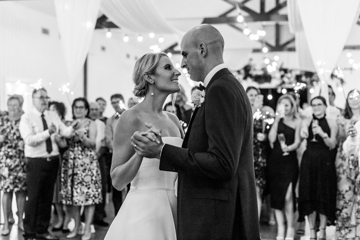 B&W image of KWH bride Samantha and husband Adam dancing at their reception surrounded by family and friends. Bride wears the Esther wedding dress.