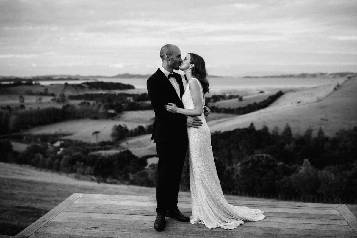 B&W image of KWH bride Tash and husband Josh sharing a kiss; bride wearing the Lola gown with a low back.