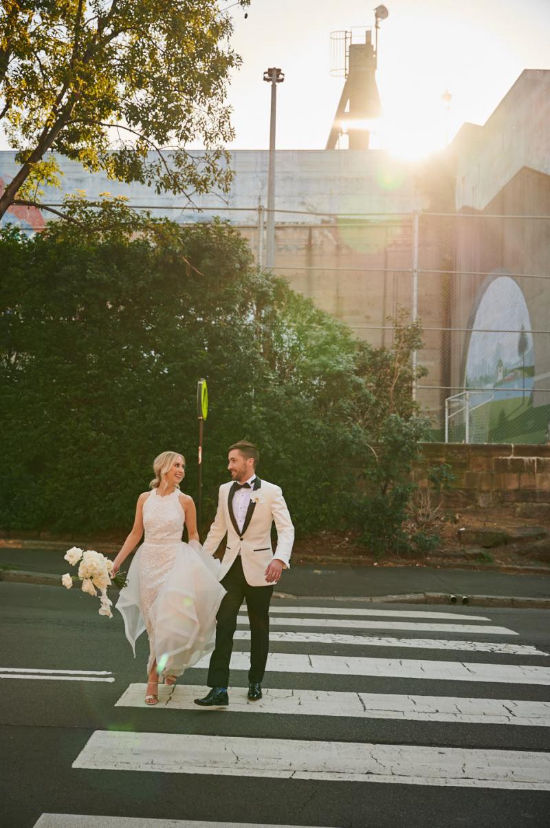 Real bride Claire wears the Cindy gown, a beaded halterneck wedding dress by Karen Willis Holmes while walking across the street with her husband.