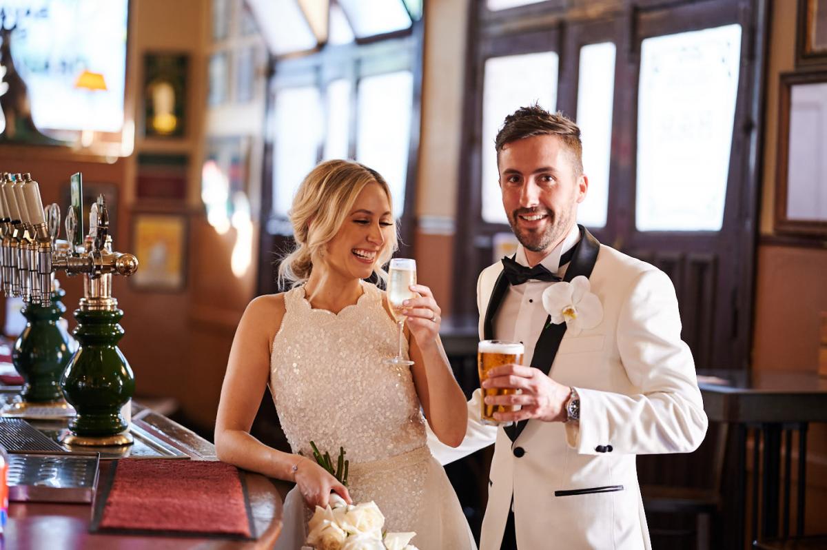 Real bride Claire wears the Cindy gown, a beaded halterneck wedding dress by Karen Willis Holmes while standing at the bar for a drink with her new husband.