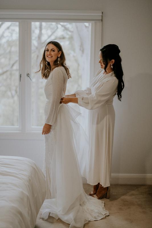 Real bride Penelope getting ready for wedding with bridesmaid, wearing the Cassie gown; a long sleeve art deco beaded wedding dress from the Luxe collection by Karen Willis Holmes.