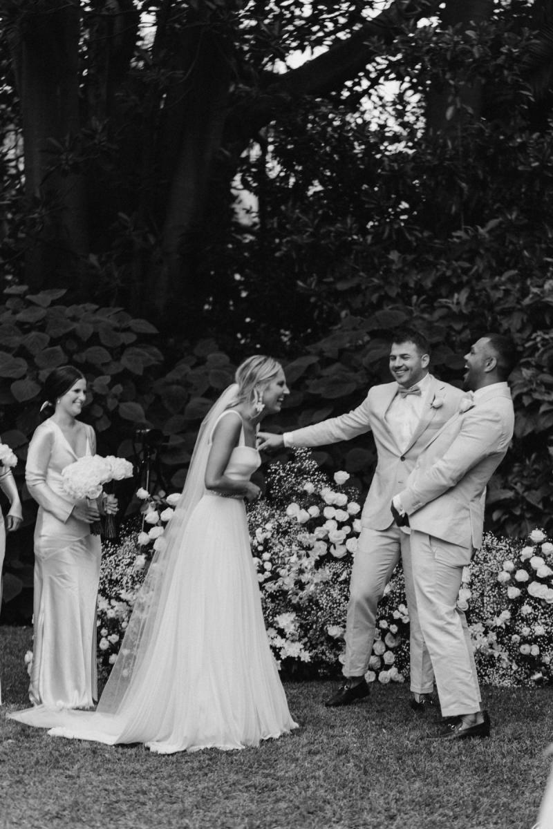 Real bride Maddi, wearing a Karen Willis Holmes gown, Daisy, laughs with her husband and wedding party.