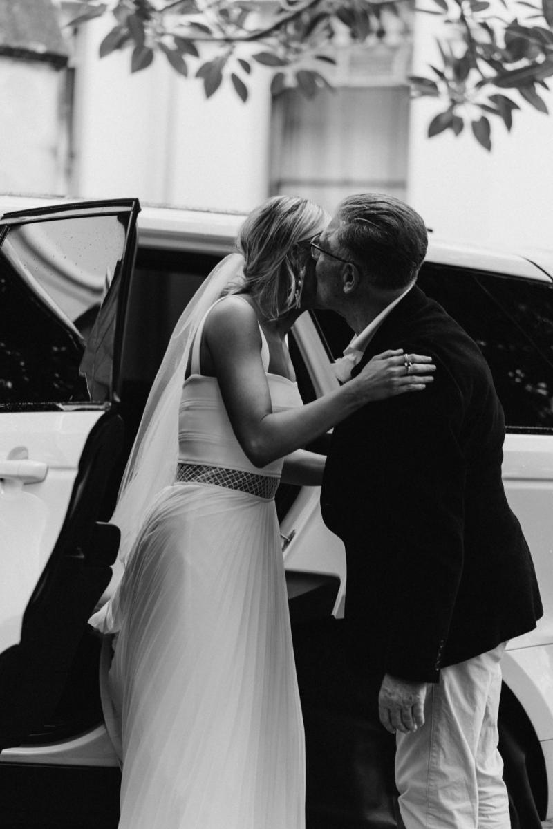 Bride Maddi, wearing the Daisy gown by Karen Willis Holmes, gives her father a kiss on the cheek as she exits the car.