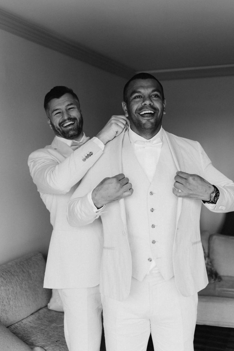 Kurtley smiles for the camera as his groomsman helps him put on his jacket for his wedding ceremony to his KWH bride Maddi.