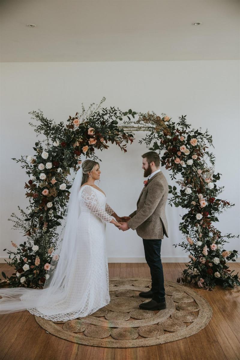Real bride Lucy wears the Bobby gown with sleeves by Karen Willis Holmes to small backyard wedding ceremony., posing with husband for small wedding ceremony.