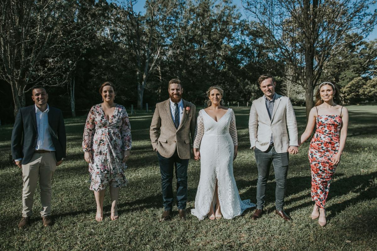 Real bride Lucy wears the Bobby gown with sleeves by Karen Willis Holmes to small backyard wedding ceremony., posing with small bridal party.
