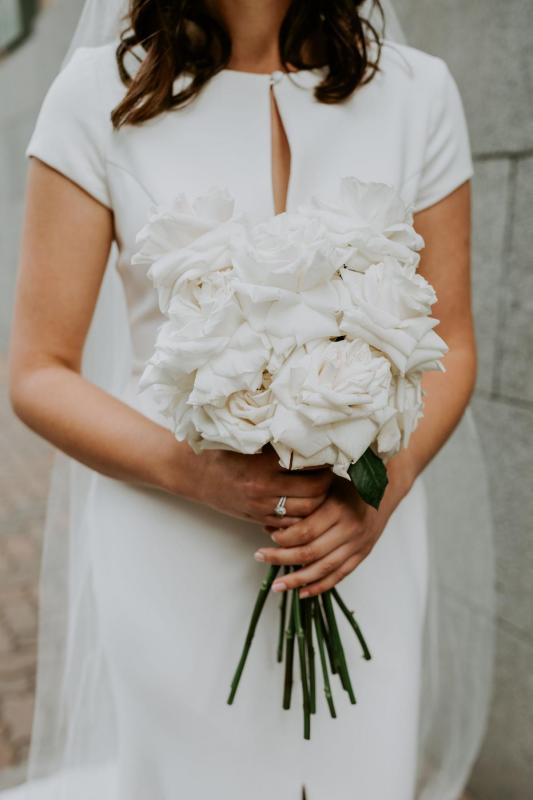 Real bride Jennifer holds a white bouquet of roses for her wedding, wearing the Clarissa gown, a simple cap sleeve wedding dress by Karen Willis Holmes.