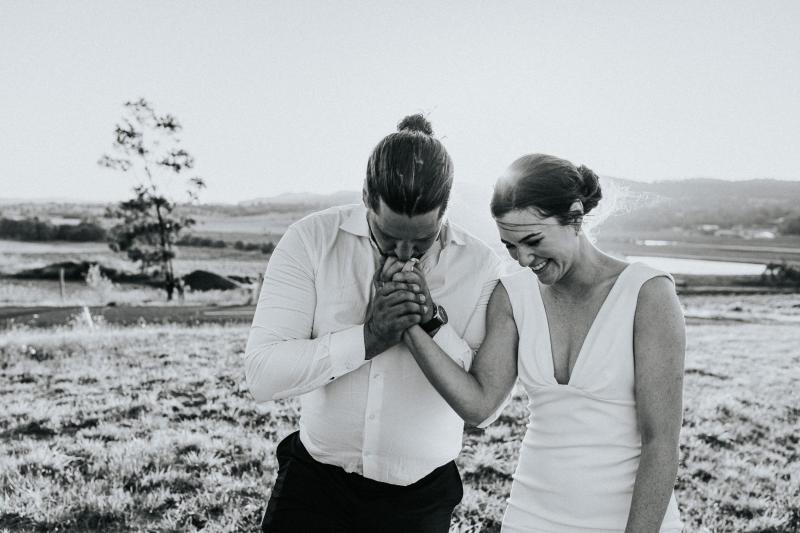 Mik kisses Real Bride, Kate's hand, in this black and white photo. Kate wears the simple Arabella gown by KWH.