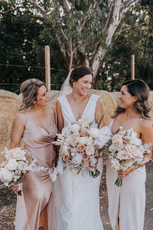 KWH real bride Kate laughs with her bridesmaids as they hold their blush and coral bouquets. Kate wears the moderns crepe Arabella dress.