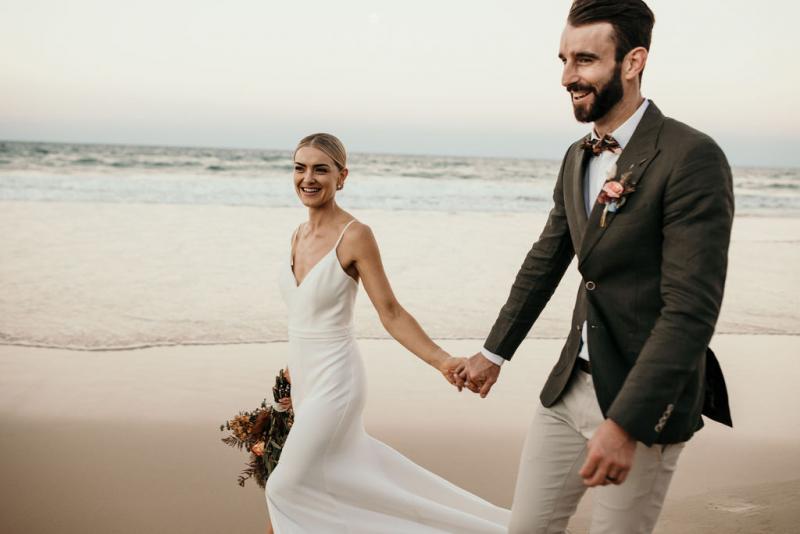Real bride Kate with her new husband at beach wedding, wearing the Caroline gown; a simple v-neck wedding dress by Karen Willis Holmes.