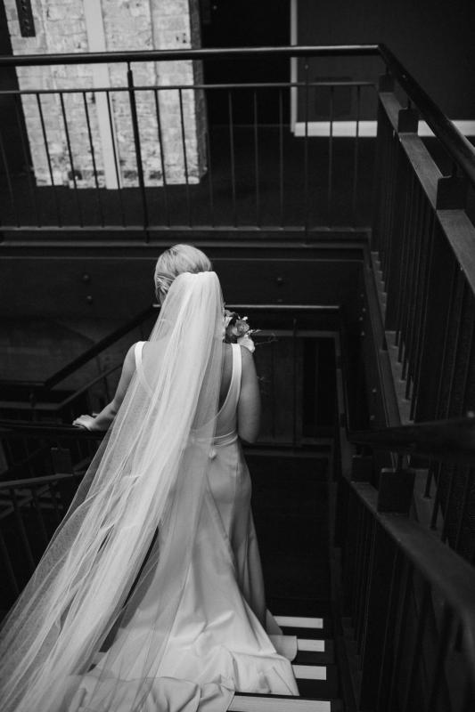 KWH real bride Eliza going down the industrial stairs at the hotel as her veil and Imogen dress trail behind her.