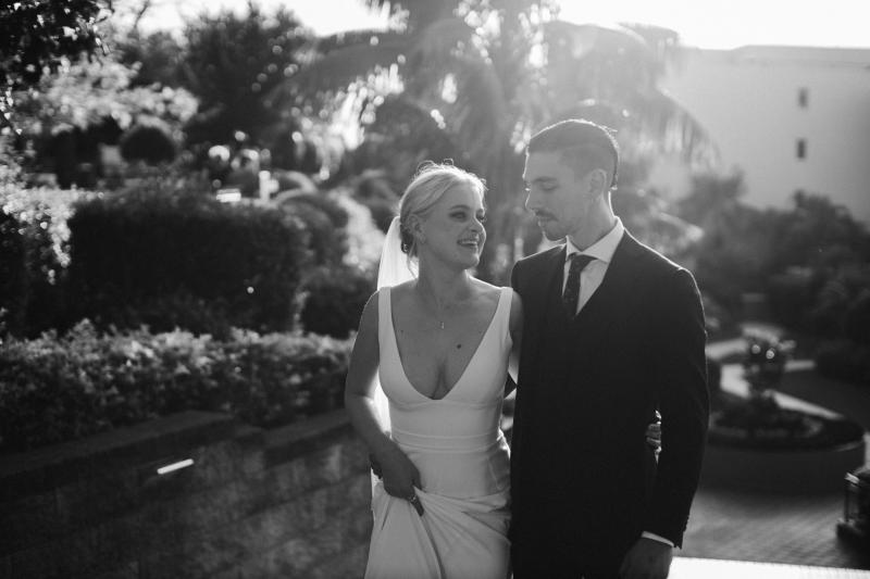 KWH real bride Eliza and Arien walk in the gardens in this B&W photo. She wears the fit and flare Imogen gown.