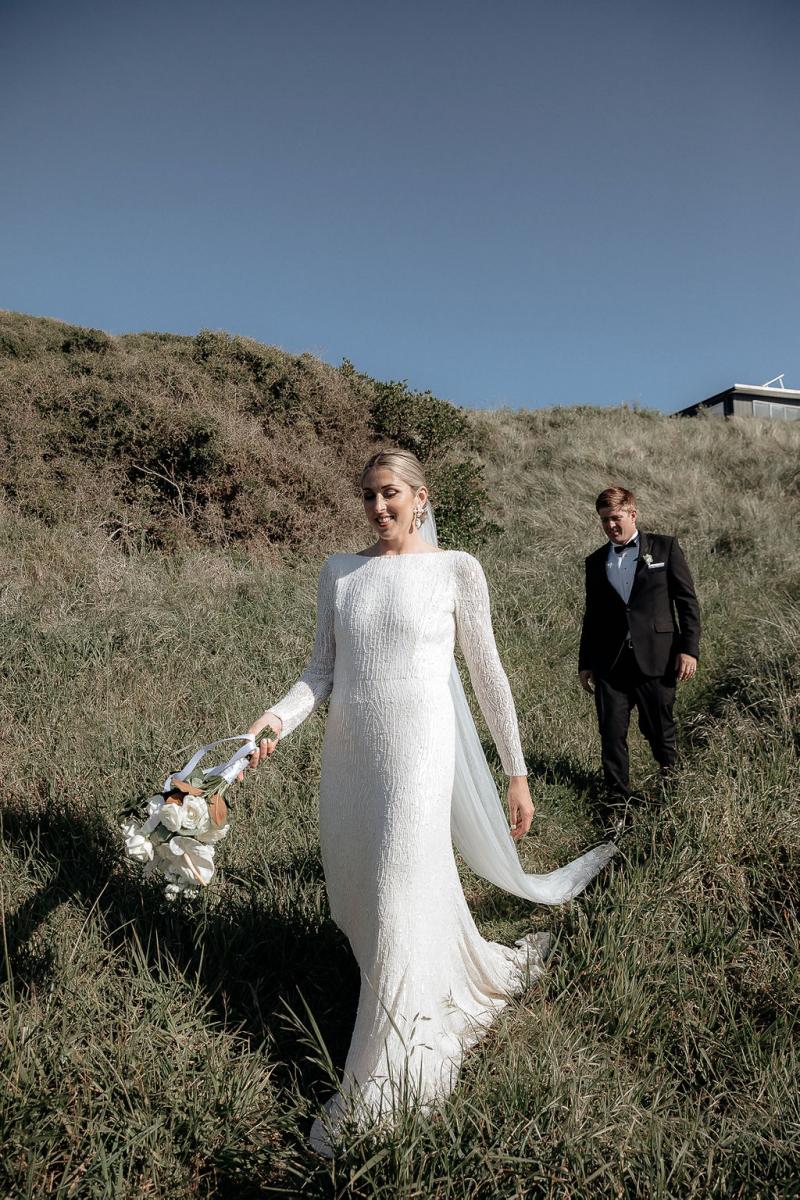 KWH real bride Hannah and Angus exchange looks while sharing a glass of champagne on the coast line. She wears the fit and flare beaded Margaretta wedding dress.