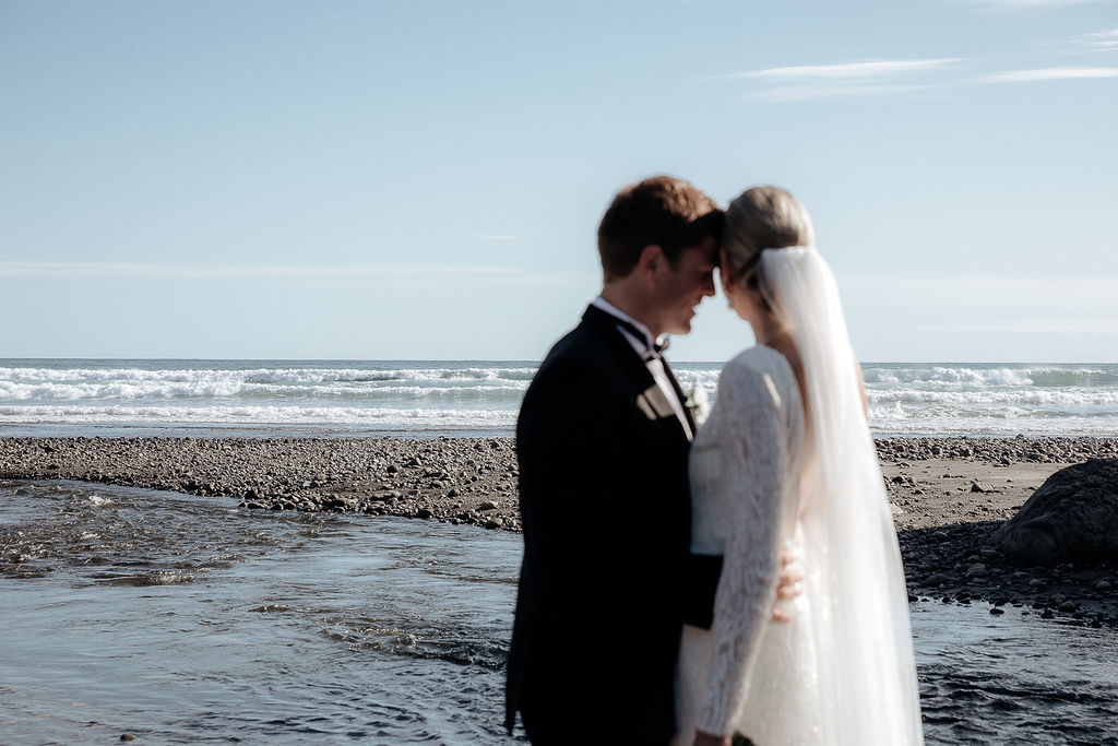 Real bride Hannah hugs Angus in front of the sea. She wears the beaded long sleeve Margaretta gown by Karen Willis Holmes.