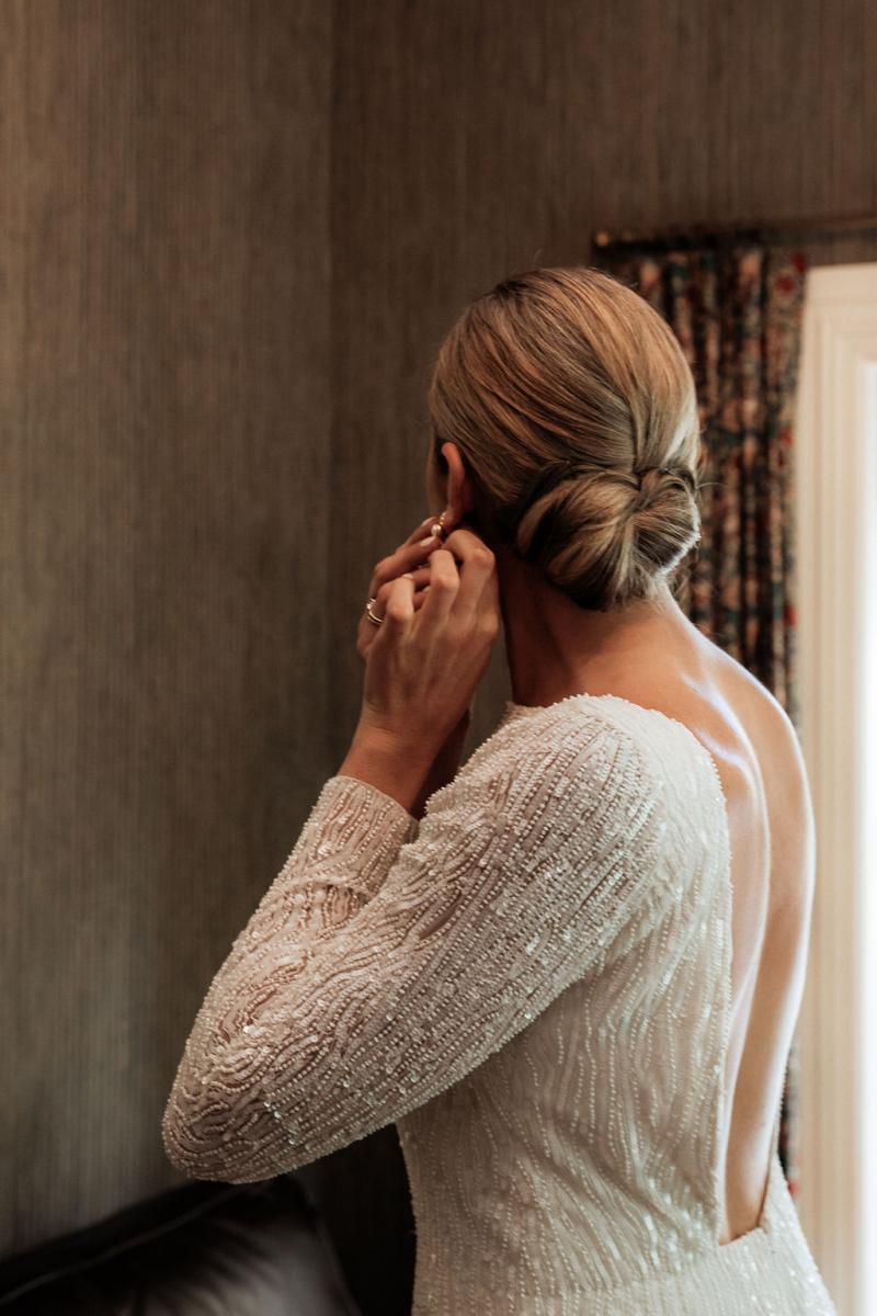 KWH Real bride Hannah adjusting her earring as she prepares for the day. She wears the simple yet stunning Margareta gown with high neckline.