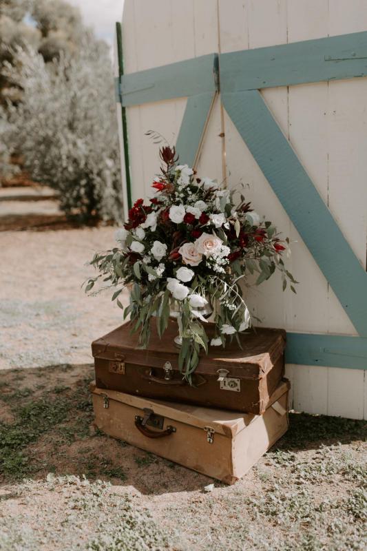 Real bride Amber's outdoor ceremony decor with two suitcases, florals, and blue and white barn door.