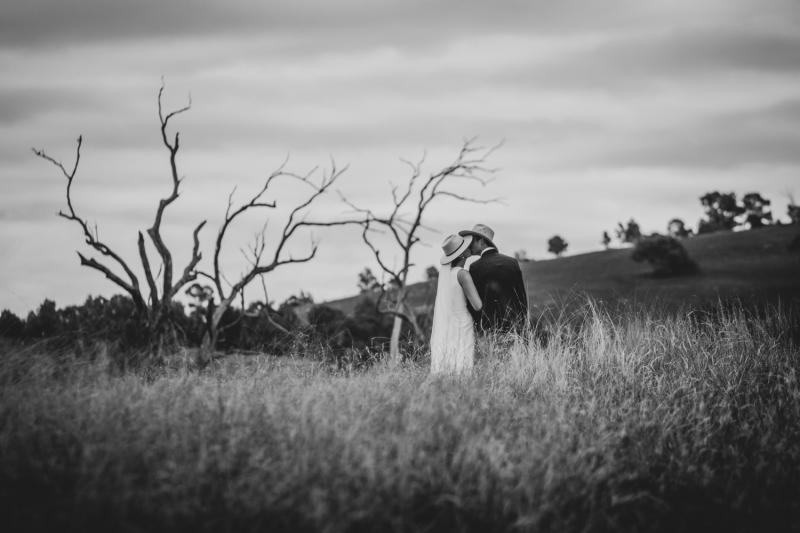 B&W photo of KWH real bride Angela kissing her husband in a field. She wears the minimalist Bridget wedding dress.