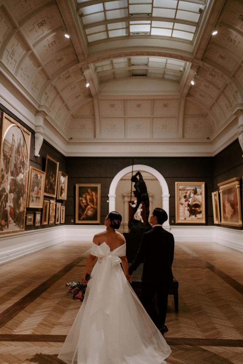 KWH real bride Sarah walks with Brian down the gallery hall in her Kitty Joni dress which has a custom bow on the back.