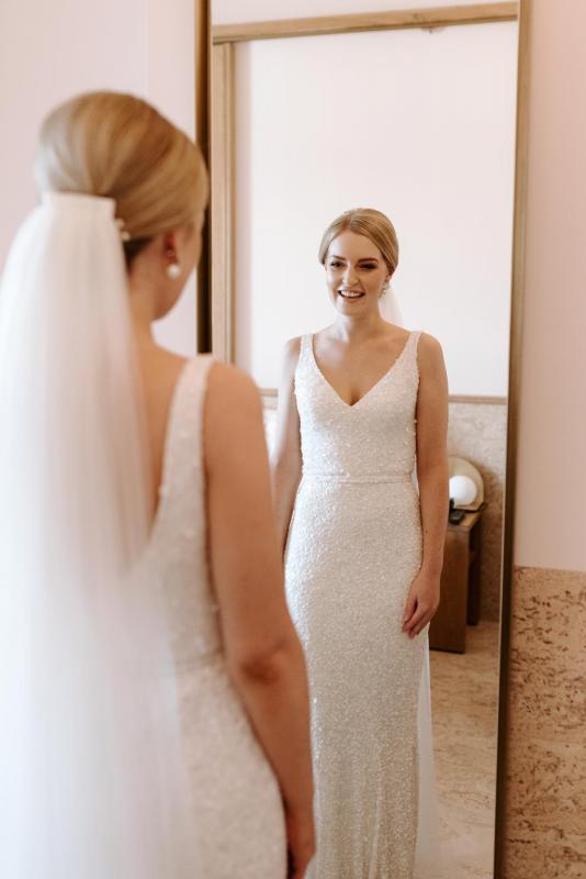 KWH real bride Katie looks into a floor length mirror in her Lola gown which features thousands of sequins and v-neck.