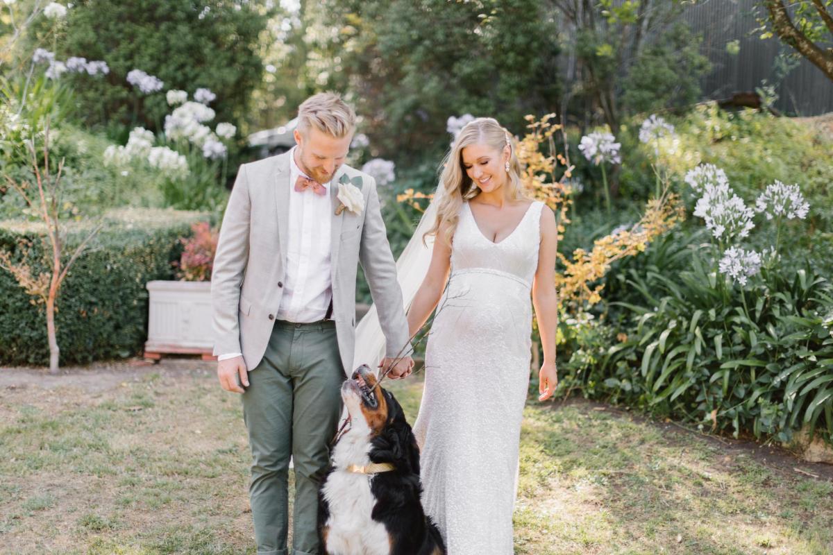 KWH real bride Bec walks with Nick with their dog between them. She wears the Olympia gown, a modern hand-beaded fitted wedding dress with V-neck