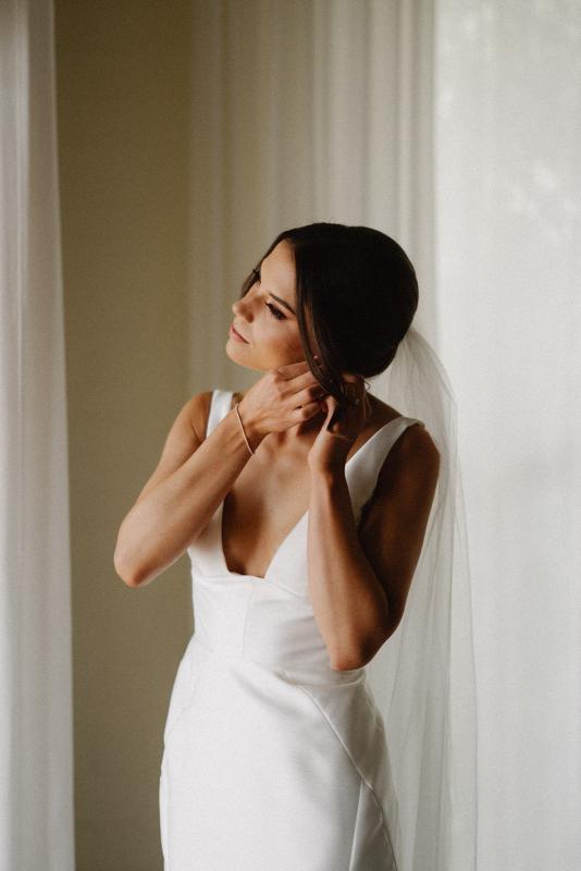 Real bride Charlotte getting ready by putting on her earrings. She wears the mix and match Leonie Alexia gown by KWH.