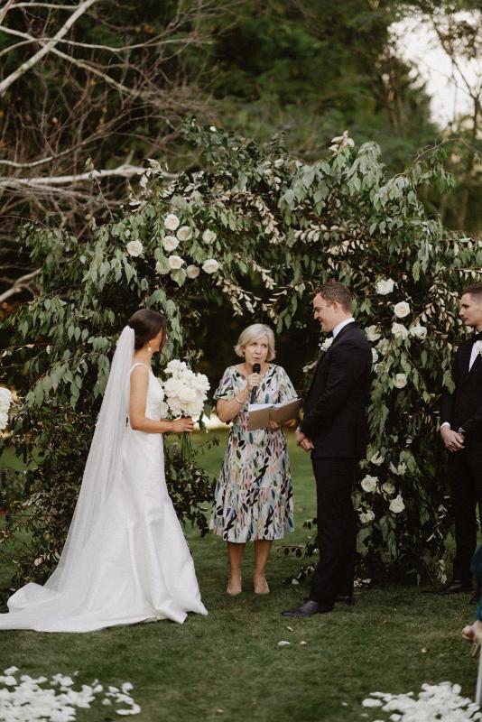 Real bride Charlotte and Myles standing at their greenery arbour for their vows. She dons the classic Leonie Alexia gown my KWH