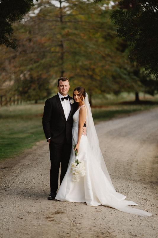 KWH real bride Charlotte wears the Leonie Alexia gown while holding her white bouquet and standing with her husband.