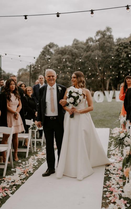 KWH real bride Elke walks down the aisle with her father. She wears the classic Blake Camille wedding dress with high split