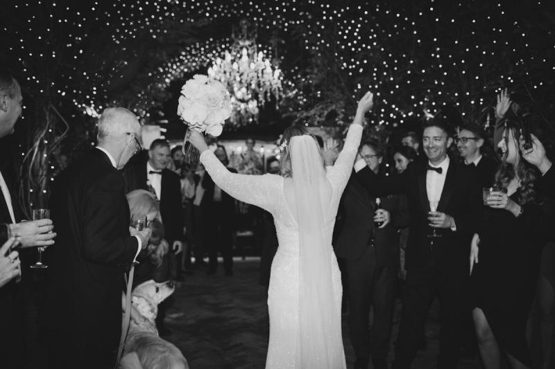 KWH real bride Emily celebrating on the dance flower as she holds her arms up. She wears the long sleeve Celine wedding dress