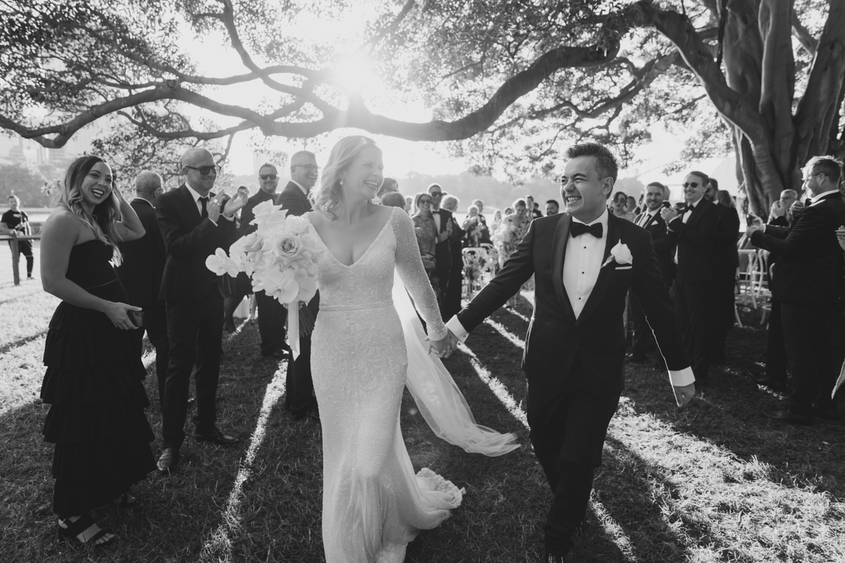 KWH real bride Emily and Mark walking down the aisle as she wears her hand beaded Celine wedding dress with v-neck.