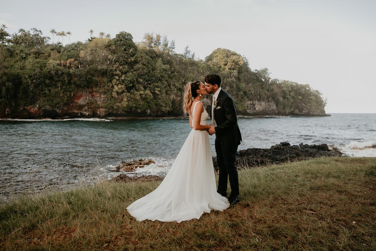 KWH real bride Jana and Garret kiss on the Hawaiian shorline. She wears the modern aline Erin and Lea wedding dress with flowy skirt and fitted bodice.
