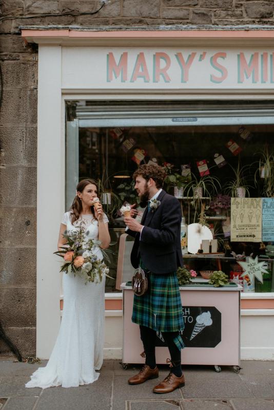 KWH real bride Mel and Robbie eat and drink out front of a darling Edinburgh cafe. She wears the modern lace Jemma wedding dress with fitted shape.