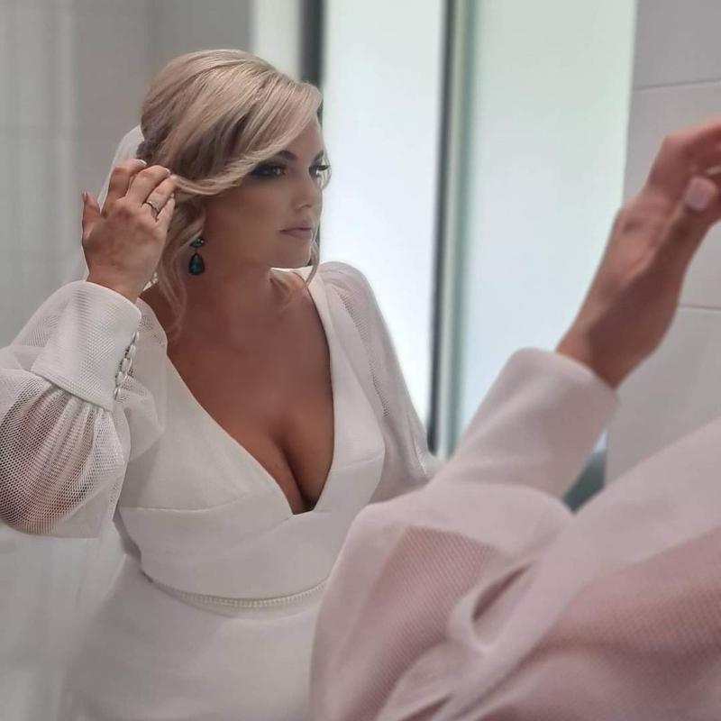 KWH real bride Caitlin looking in the mirror. She wears the contemporary Penelope wedding dress with cufff sleeves.