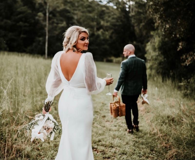 KWH real bride Caitlin and Eoin walking as he carries a case and she wears the low back Penelope wedding dress.