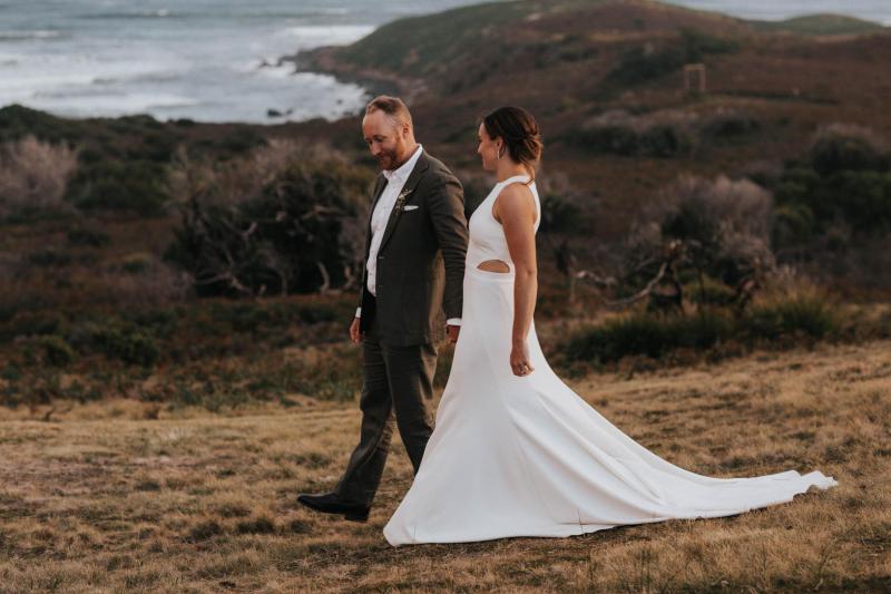 KWH real bride Ashleigh walking with simon on the cliffs of Tasmania while she wears her high neckline Bridget wedding dress with simple train.