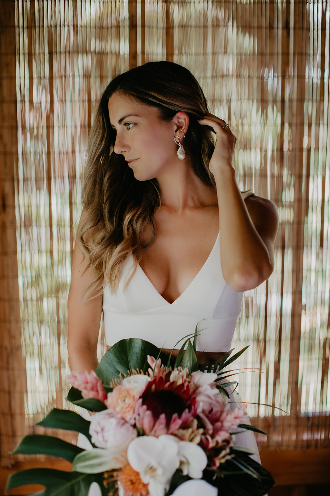 KWH real bride Jana standing in a wooden room with her native Hawaiian bouquet from Grace Flowers. She wears the v-neck Erin bodice paired with the aline Erin skirt.