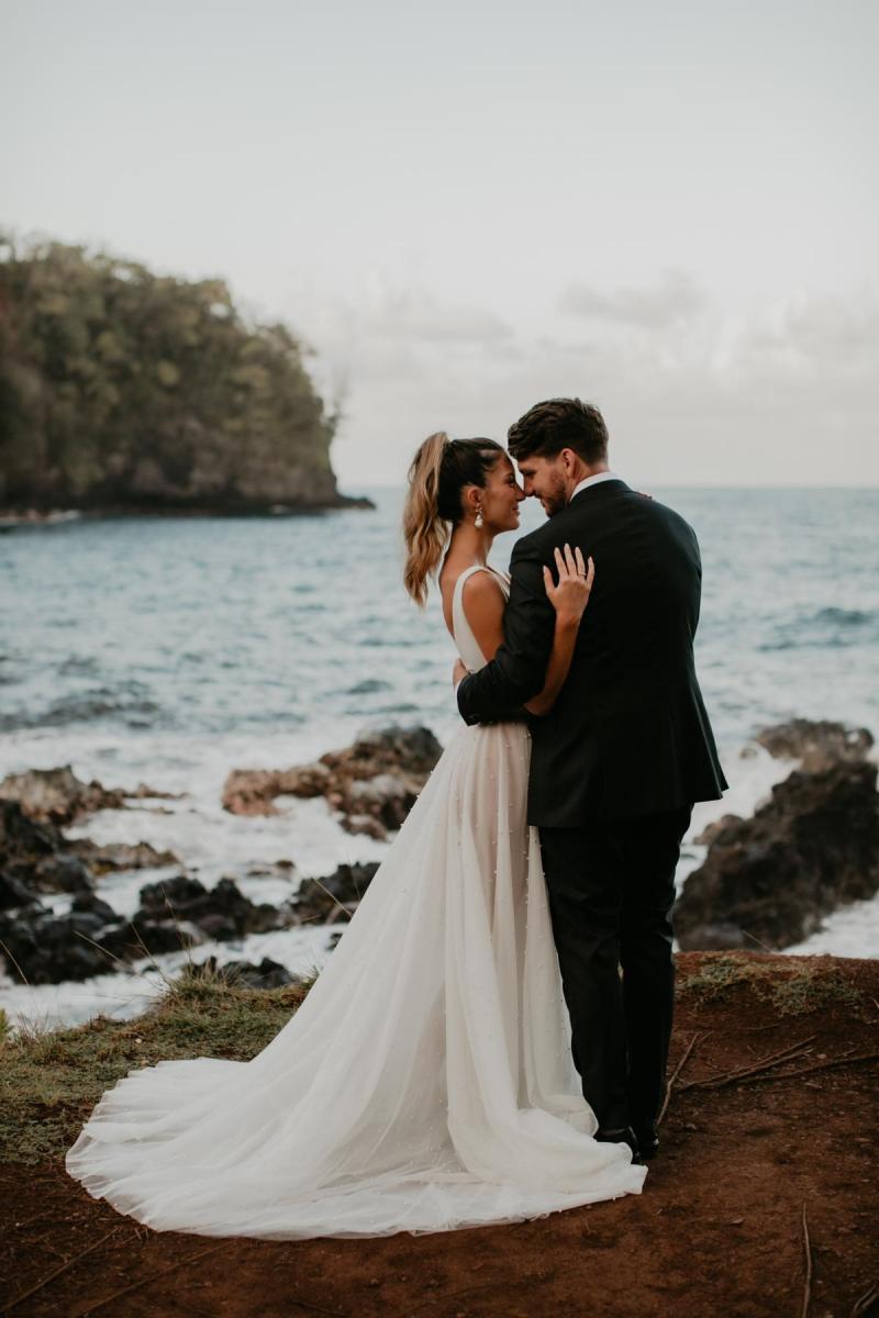 KWH real bride Jana looking into Garret's eyes as they stand on the shores of the Hawaiian beaches. She wears the modern Erin and Lea wedding dress to her intimate elopement.