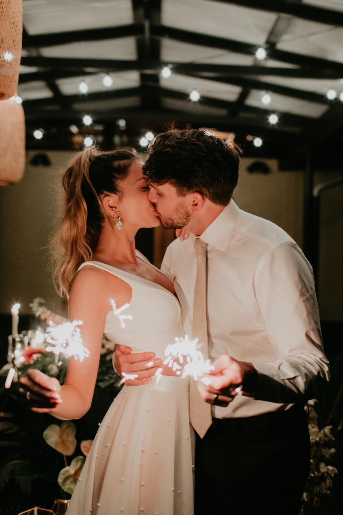 KWH real bride Jana sharing a kiss with her new husband Garret by the glow of their sparklers. She wears the effortless Erin and Lea wedding dress combo.