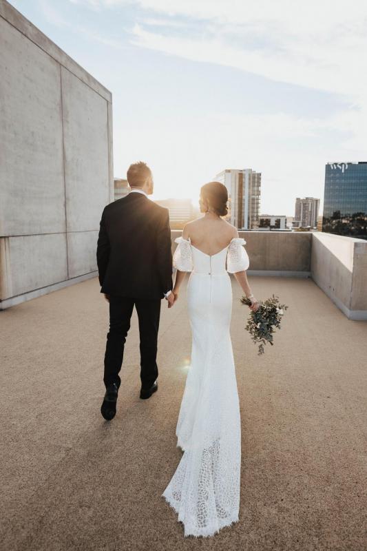 KWH real bride Tess and Liam walk into the sunset atop the Calile hotel. The picture shows her stunning v-back, Vivienne wedding dress with long train.