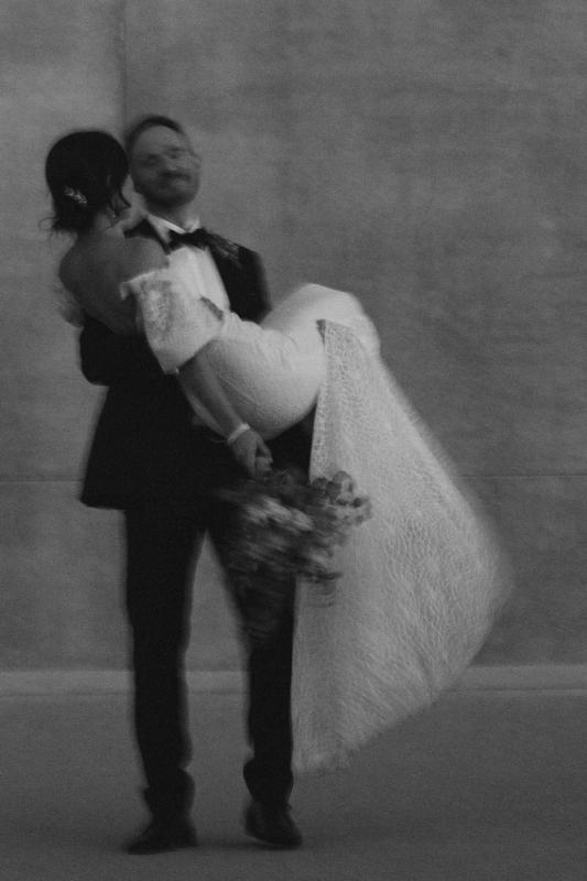 B&W image of KWH real bride Tess being held by Liam. She wears the Vivienne wedding dress with simpel lace.