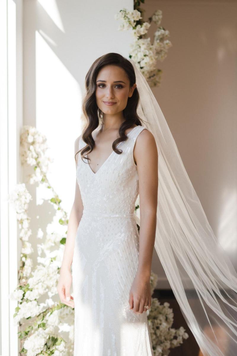 KWH real bride Georgie stands in the glow of the window in her stunning beaded Fontanne wedding dress with V-neck and fit and flare silhouette.