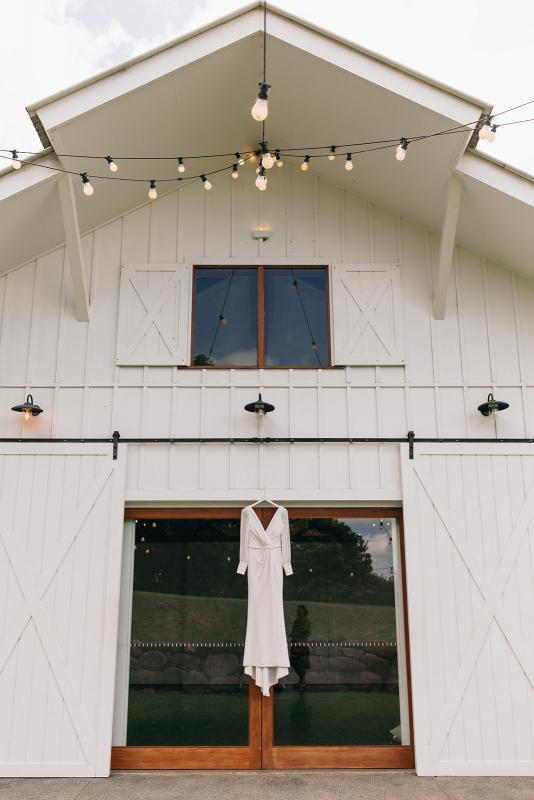 KWH real bride Rebekah's Nikki wedding dress hanging on the white barn door.